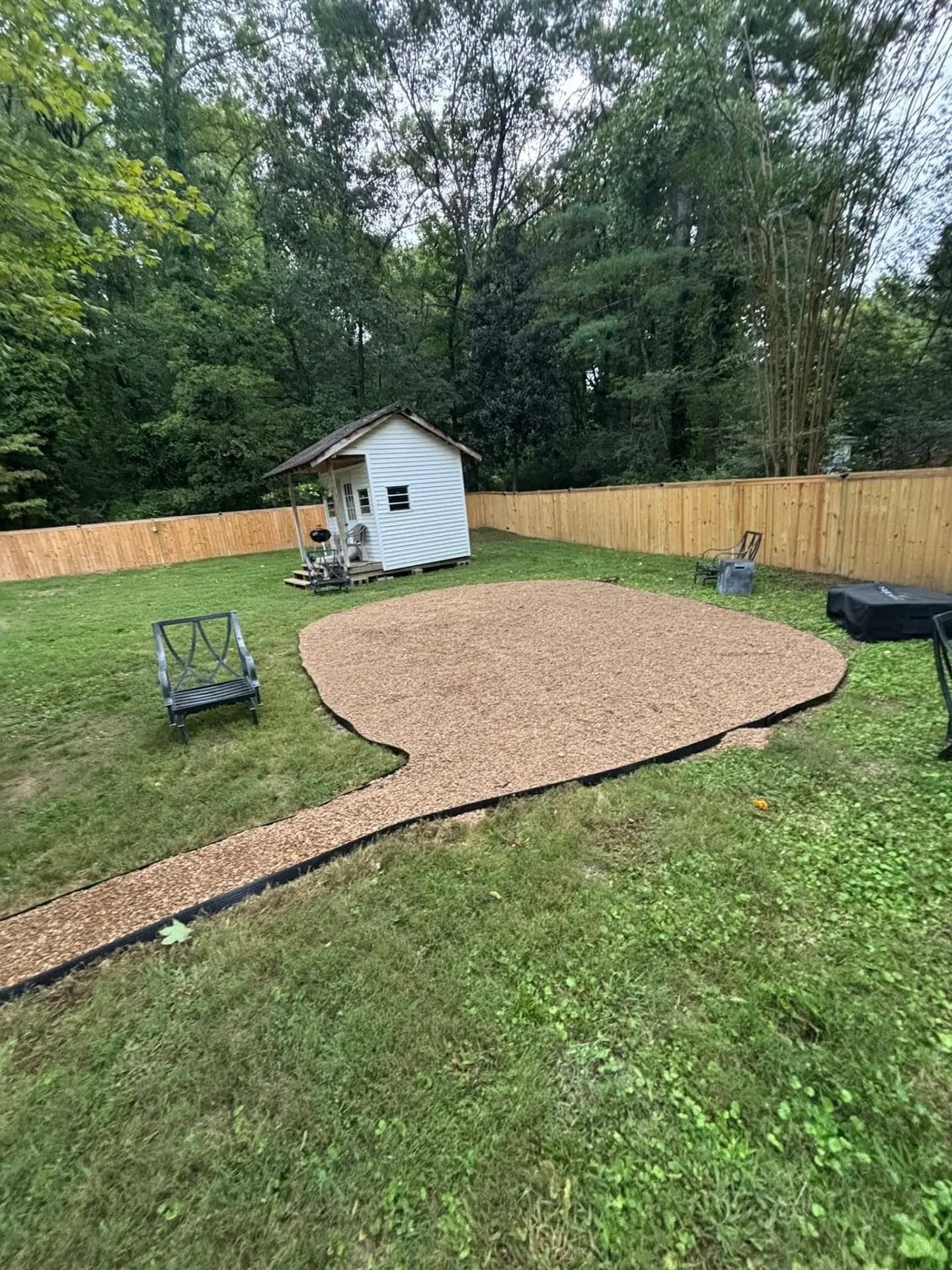 Backyard gravel patio with edging installed around a shed